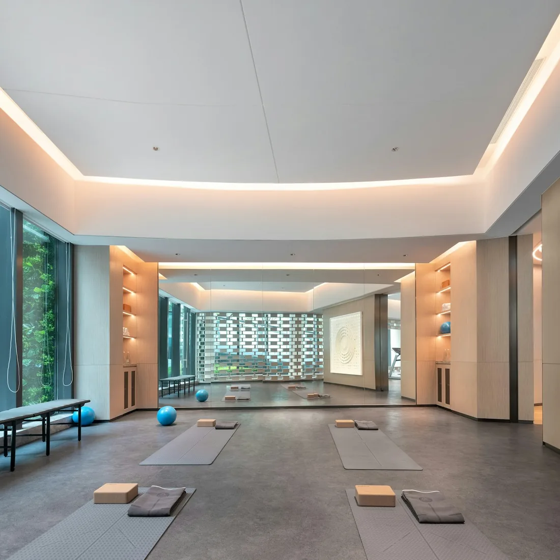 Sala de yoga vacía con esterillas extendidas, bloques y mantas sobre un suelo continuo, con luz natural entrando por ventanales laterales